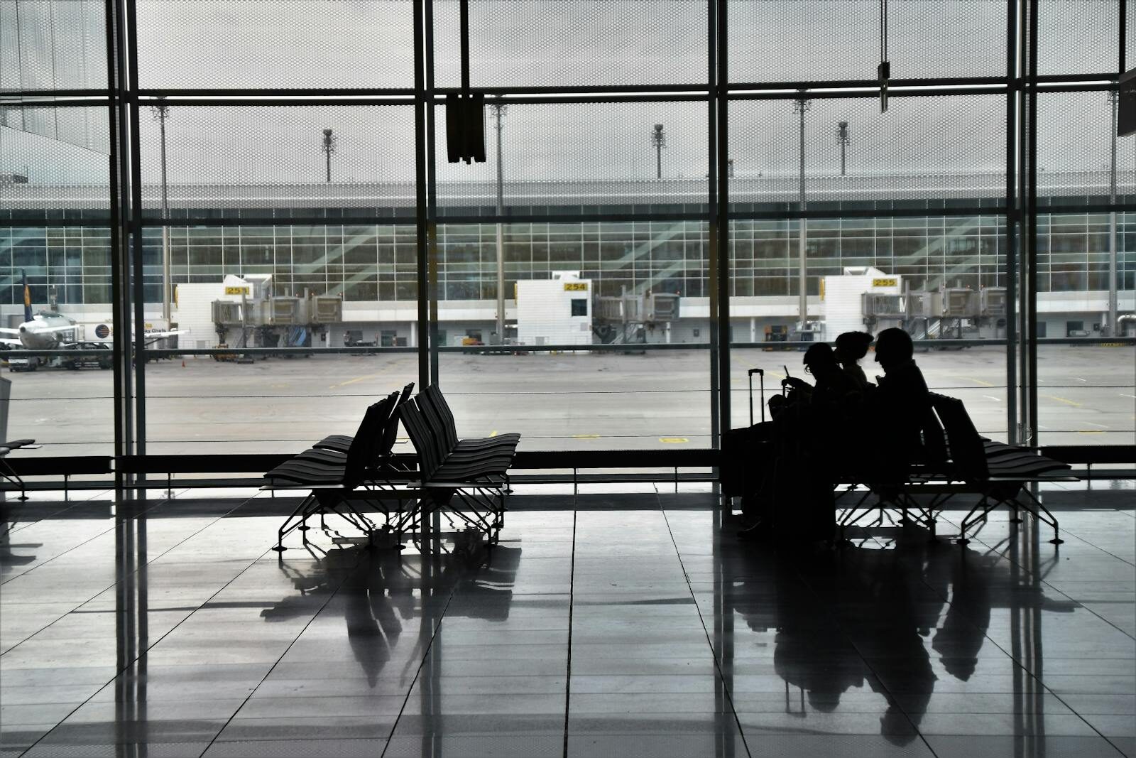 Silhouette of unrecognizable passengers sitting on chairs with luggage near window and waiting for flight