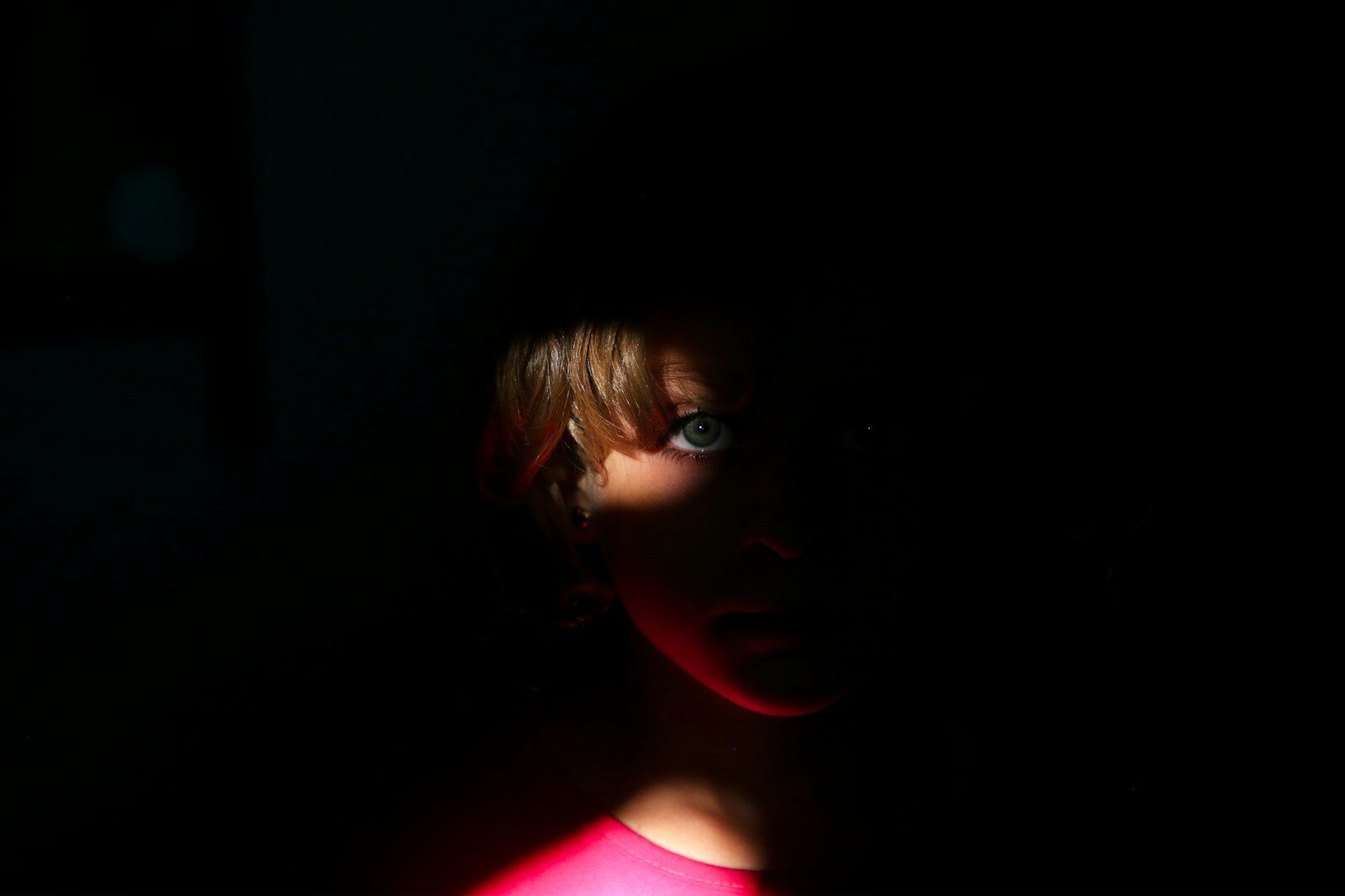 A young girl in a pink dress in a dark room